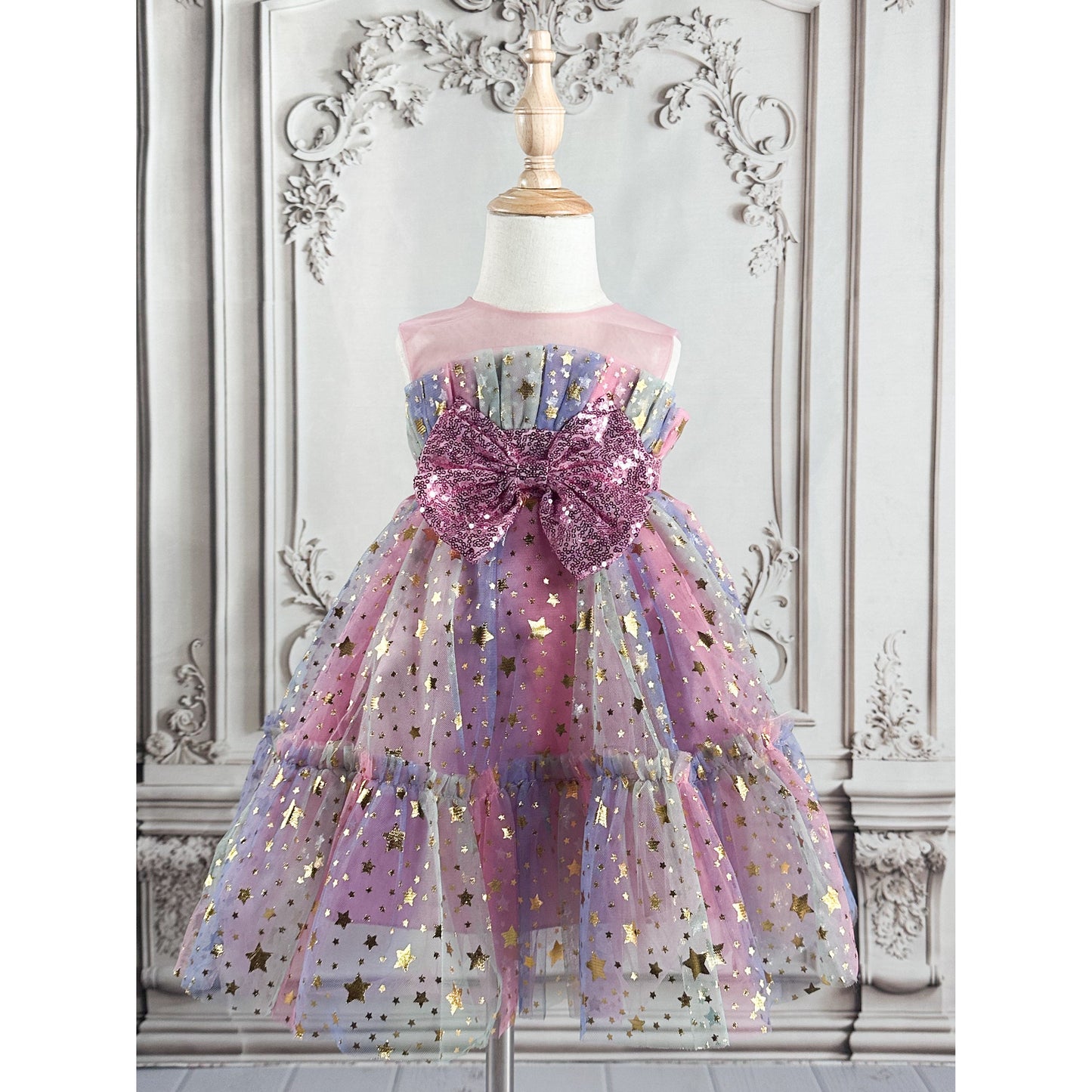 pink tulle dress with pink bow with sequins in the front, gold stars throughout the dress, see through pink mesh at the very top of dress, has light purple, light green colors