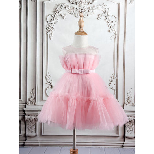 A pink tulle princess dress displayed on a mannequin stand, featuring a pleated top, bow belt at the center, and a sleeveless