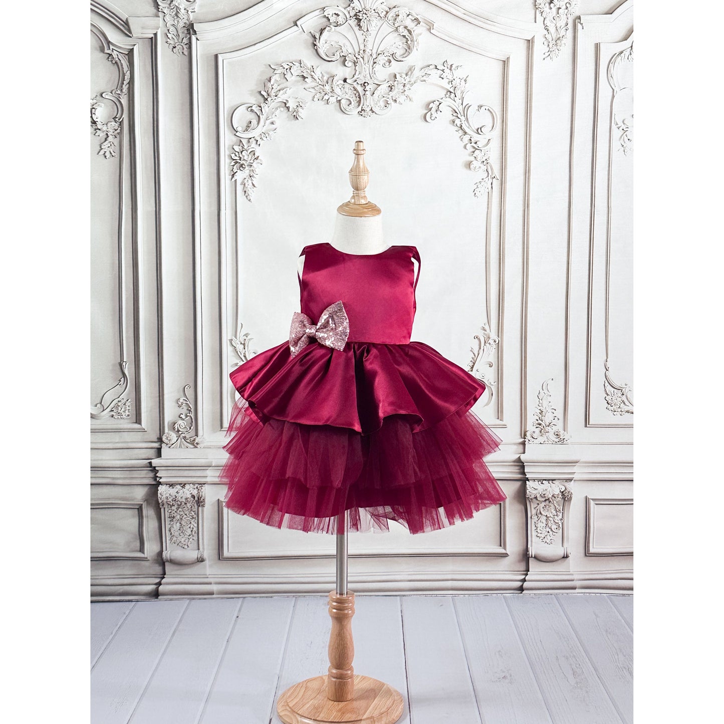 maroon dress with maroon tulle, a light pink with gold sequin bow displayed on a mannequin against an elegant background.