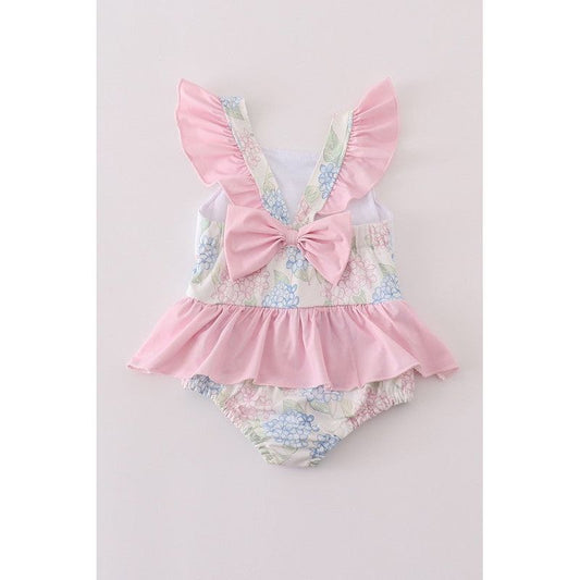 A pastel pink toddler girl's swimsuit with ruffled detailing and pastel pink bow on the back side