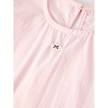 Pink outfit with top that has bubble sleeves and skirt that has elastic waist and ruffles at the bottom of skirt on a hanger, accompanied by a matching hair scrunchie  with white lace around on a light gray background. close up of small black bow design button sewed to front of top