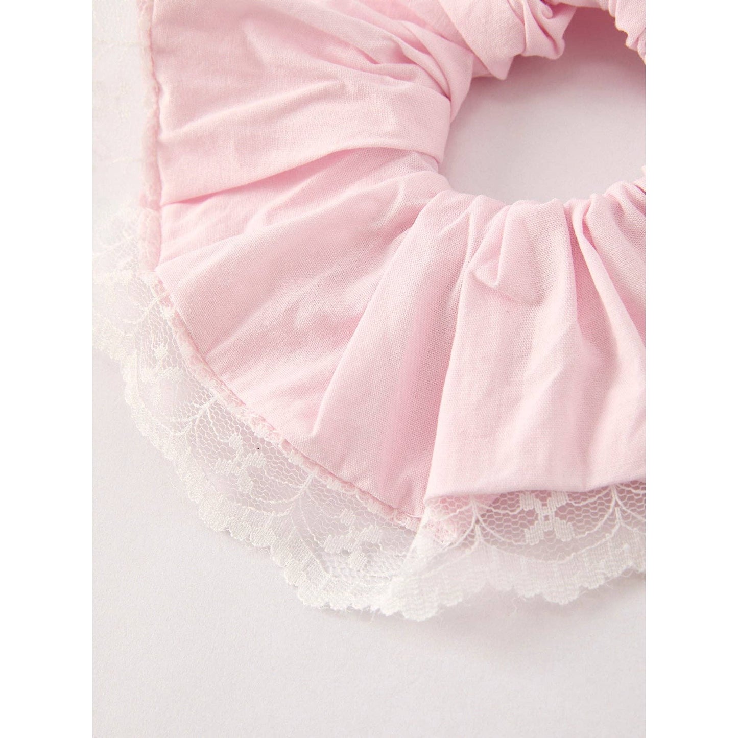 Pink scrunchie with lace trim on a light gray background