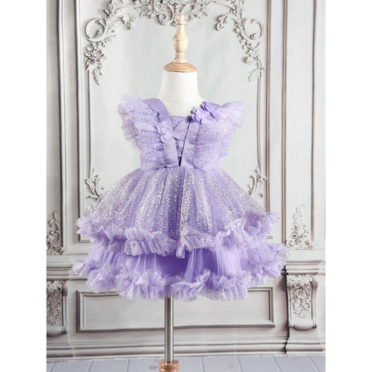A light purple girl's dress with delicate butterfly patterns at the top, silver linear decor throughout the dress, and purple tulle, displayed on a wooden stand with an ornate white background, back side