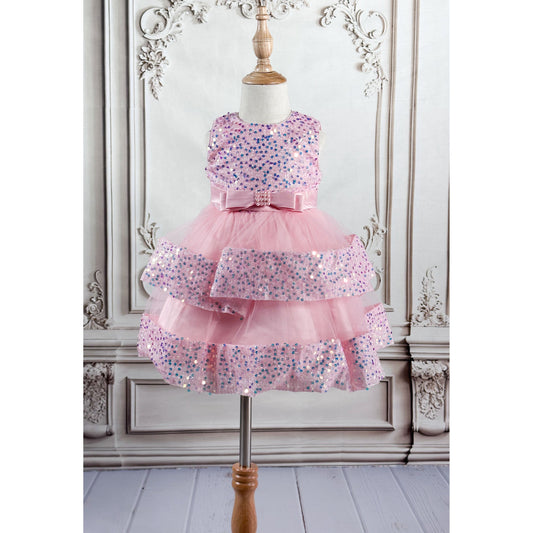 A light pink tulle dress with sequins and a bow belt, displayed on a wooden stand with an elegant neutral colored background, closer view